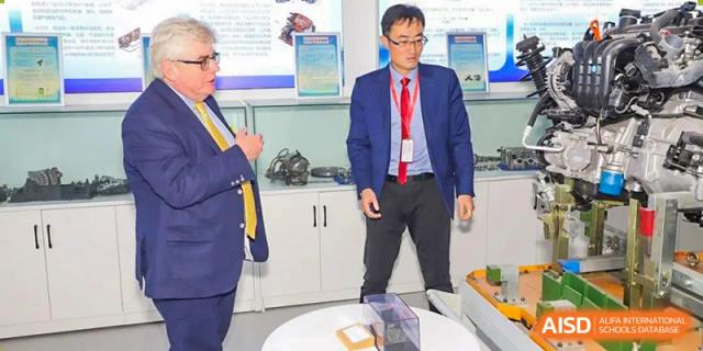 An administrator or teacher from Yancheng Foreign Language School in a suit and red tie standing in an office or presentation area.