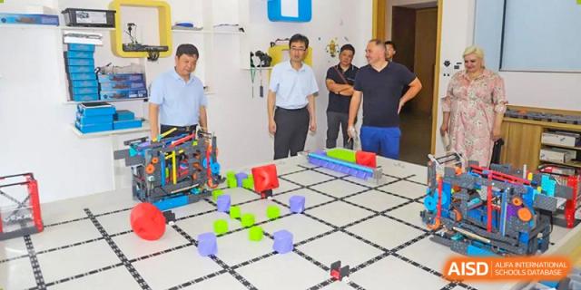 Yancheng Foreign Language School students and staff observing a demonstration of a robotics or coding challenge setup on a grid floor.