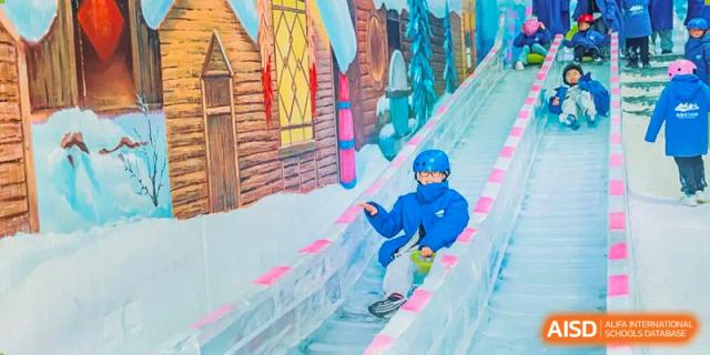 A Yancheng Foreign Language School student in a blue snowsuit sliding down a colorful indoor snow slope or tubing lane.