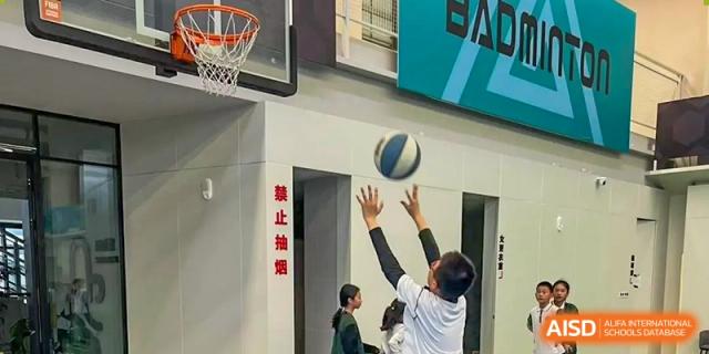 A Yancheng Foreign Language School student taking a basketball shot in an indoor gymnasium with a "No Smoking" sign visible on the wall.