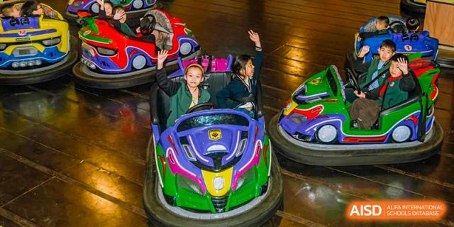 Two Yancheng Foreign Language School students riding a brightly colored, purple and yellow bumper car in an indoor amusement area.