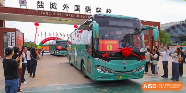 A Yancheng Foreign Language School tour bus or school shuttle, decorated with festive ribbons and banners, parked in front of a building.