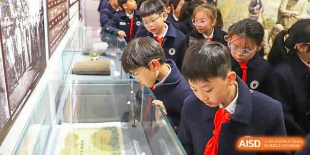 A group of Yancheng Foreign Language School students in school uniforms looking intently at exhibits in a museum or display case.