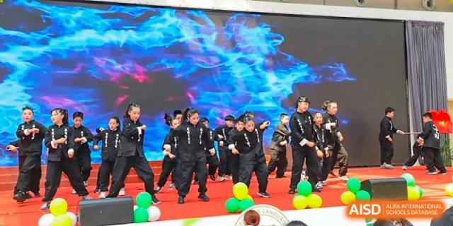 A large group of Yancheng Foreign Language School students performing a group dance or theatrical act on stage, many dressed in black uniforms.