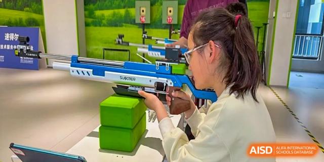 A Yancheng Foreign Language School student aiming a blue target rifle at green blocks during a sports or educational activity.