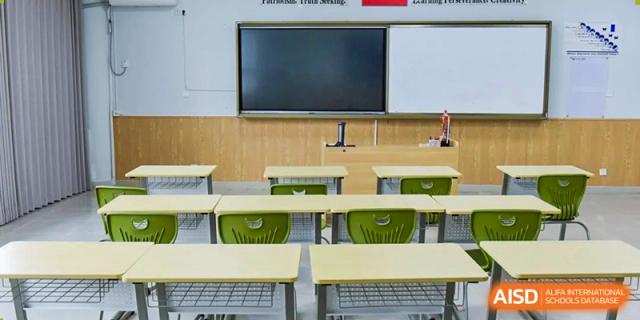 Empty classroom with rows of light green desks and chairs facing a large blank whiteboard or screen, Fuyuan British American School.