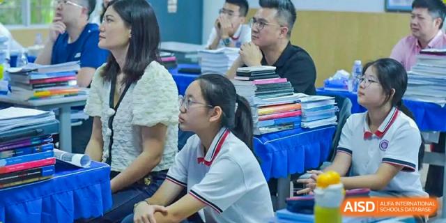 A female student in a white shirt and glasses attentively watching a presentation or speaker during a class or event, Fuyuan British American School.