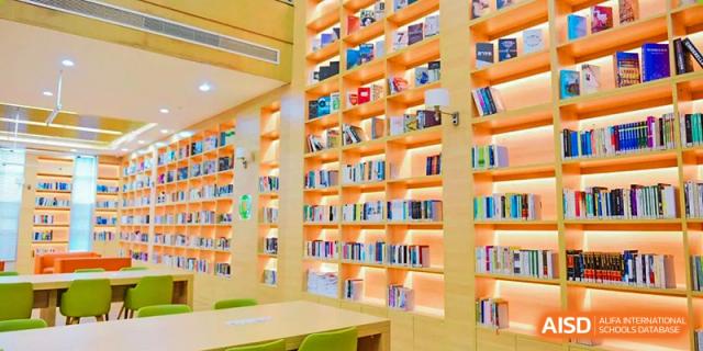 A brightly lit, modern school library or resource center with high shelving full of books, Fuyuan British American School.