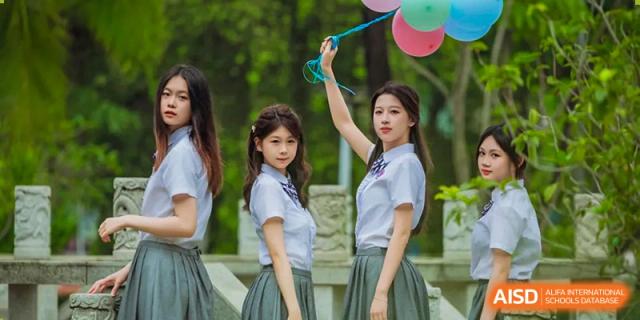 Two female students in school uniform posing outdoors, with one holding a phone above her head, Fuyuan British American School.