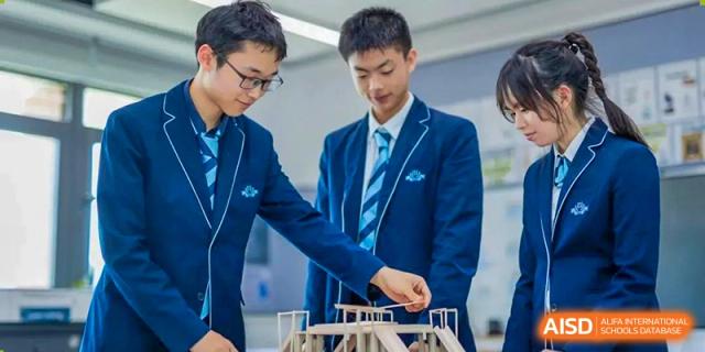 Two male students in blue school blazers and ties working on a model structure for a project at ISA Wuhan International School.