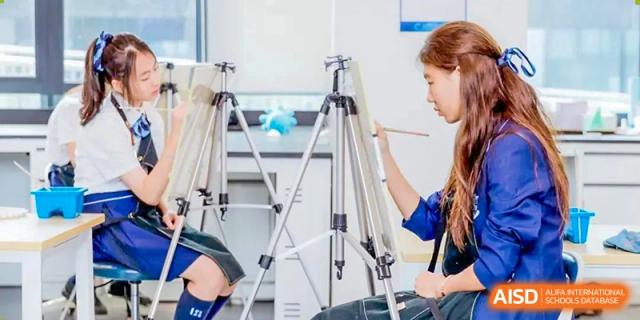 A student setting up a tripod, possibly for a photography or art class, in a bright studio at ISA Wuhan International School.
