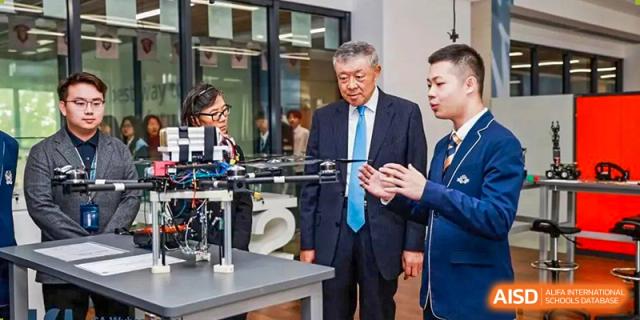 An older man in a suit (likely a guest or official) observing a technology project, possibly a drone, presented by students at ISA Wuhan International School.