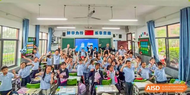 A large group of excited students and teachers gathered in a classroom or small auditorium with a banner in Chinese script at ISA Wuhan International School.