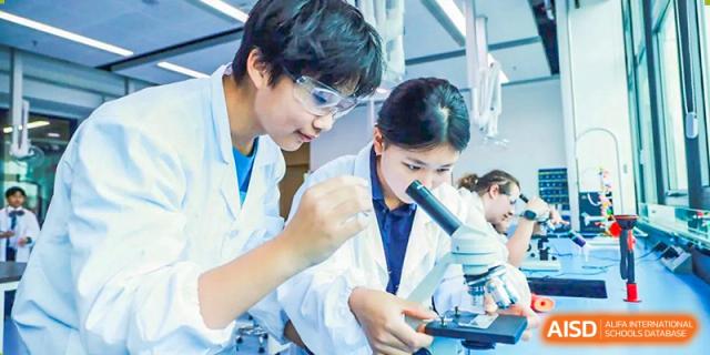 Two students in white lab coats, one looking through a microscope, working together in a science lab at ISA Wuhan International School.