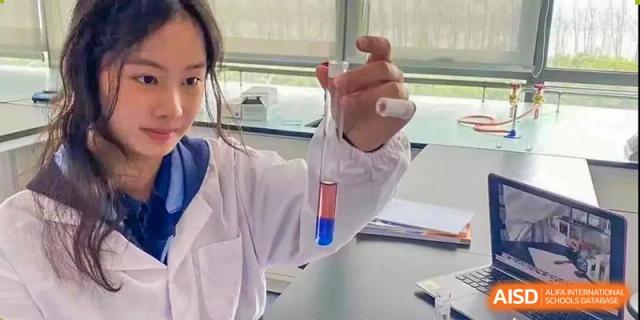 A close-up of a student in a lab coat holding up a test tube with a blue and clear solution in a science experiment at ISA Wuhan International School.