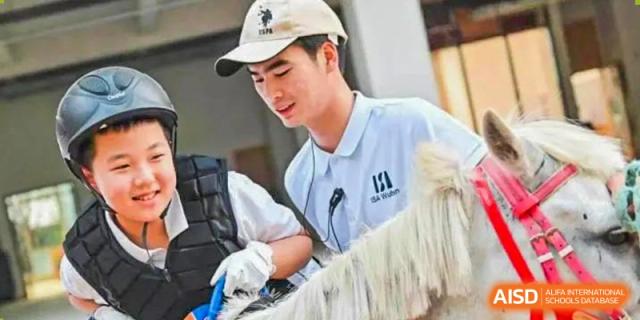 A young man in a white polo shirt and baseball cap, possibly a student, interacting with an animal, with the text "ISA Wuhan International School" at the end.