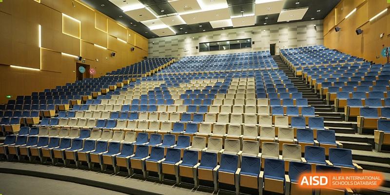 An image of a large, empty auditorium or concert hall with rows of blue and gray seating at ISA Wuhan International School.