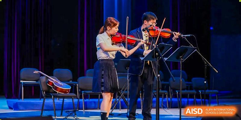 A male and female student playing the violin together during a performance at ISA Wuhan International School.