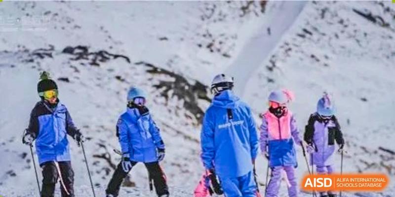 Two individuals wearing blue ski jackets and helmets, likely students or staff, on a snowy slope during a ski trip or activity organized by ISA Wuhan International School.