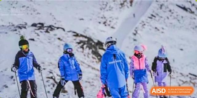 Two individuals wearing blue ski jackets and helmets, likely students or staff, on a snowy slope during a ski trip or activity organized by ISA Wuhan International School.