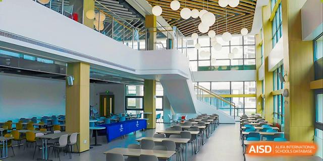 A large, modern school atrium or cafeteria area with tables, a staircase, and a bright open design at ISA Wuhan International School.
