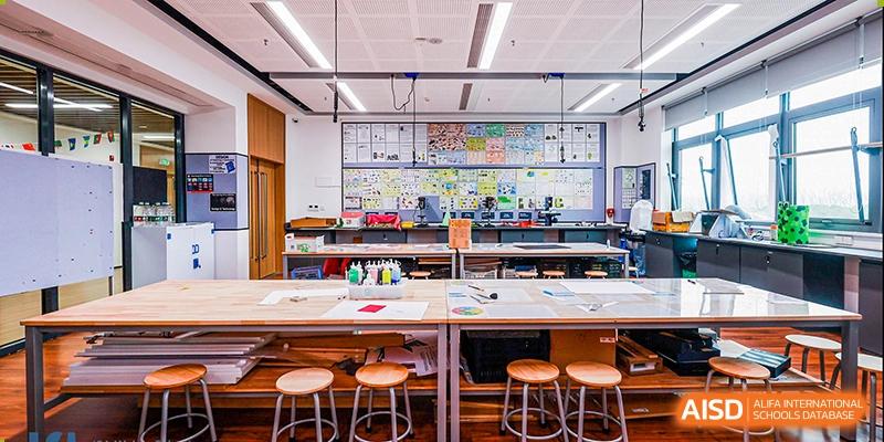 A brightly lit, spacious art and design studio with worktables, stools, and student art projects displayed on the back wall at ISA Wuhan International School.