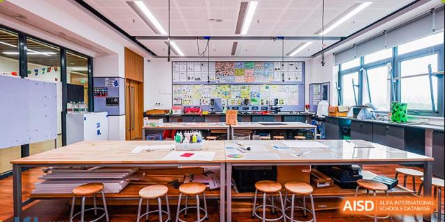 A brightly lit, spacious art and design studio with worktables, stools, and student art projects displayed on the back wall at ISA Wuhan International School.