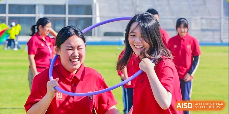 Two cheerful students, a boy and a girl, laughing while participating in an outdoor activity with a hula hoop at ISA Wuhan International School.