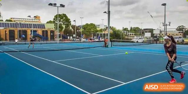 A wide view of a blue outdoor tennis court with a student or coach practicing in the background at ISA Wuhan International School.