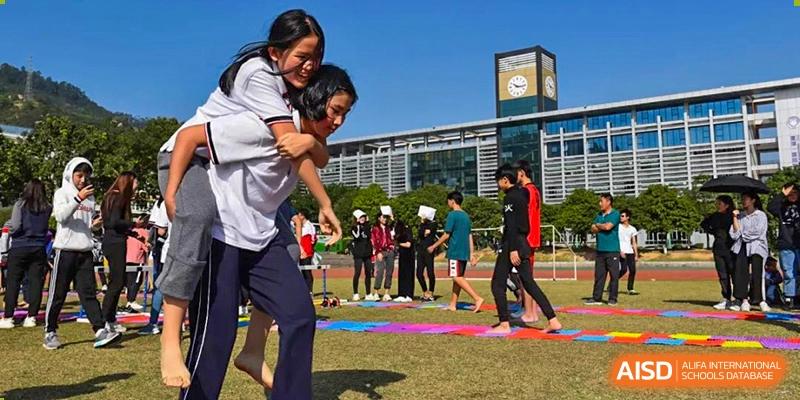 Two students from Fuyuan British American School participating in an outdoor relay race, with one student giving another a piggyback ride.