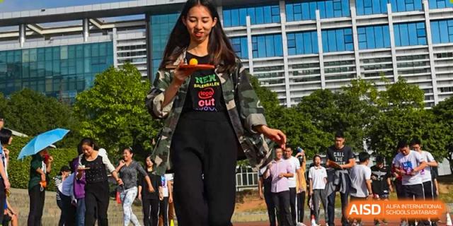 A female student from Fuyuan British American School balancing a ping pong ball on a paddle during an outdoor activity day.