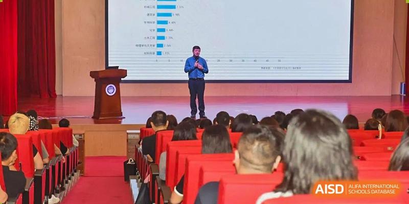 A speaker standing on a stage, addressing an audience of students and staff at a Fuyuan British American School assembly.