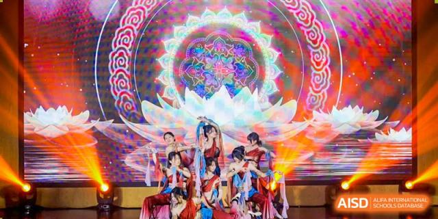 Students from Fuyuan British American School performing a synchronized dance on stage with colorful, elaborate background visuals.