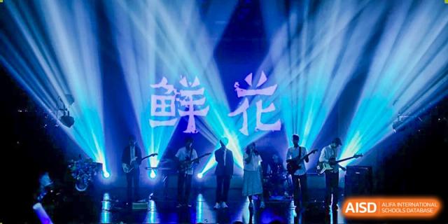 The school band from Fuyuan British American School performing live on a stage with bright blue and white lighting and Chinese characters displayed.