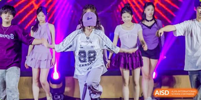 A student from Fuyuan British American School performing a hip-hop or modern dance on stage, wearing an oversized jersey.
