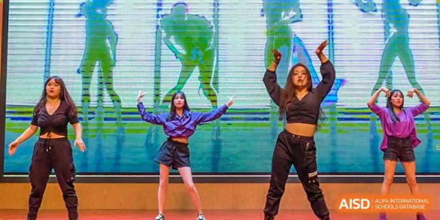 Two students from Fuyuan British American School performing a dance in black and purple outfits on a brightly lit stage.