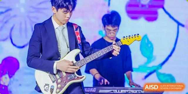 Two male students from Fuyuan British American School playing electric guitar and keyboard during a band performance.