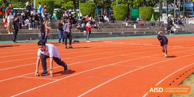 A student from Fuyuan British American School running on the track during a school sports event, with spectators in the stands.