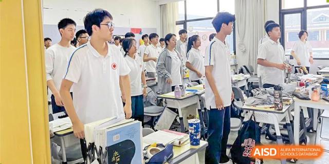 Students wearing white polo shirts standing respectfully next to their desks in a bright classroom at Glocal Elite International School.