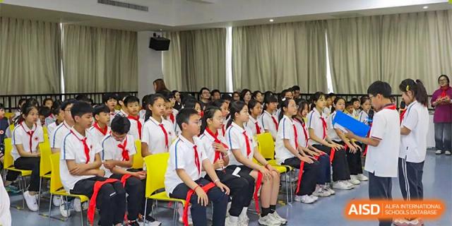 A large group of students in school uniforms sitting attentively in yellow and black chairs during an indoor assembly or lecture at Glocal Elite International School.