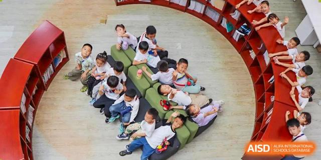 Younger students relaxing and reading on a large, custom-designed green beanbag bench in a comfortable, bright area of the library at Glocal Elite International School.