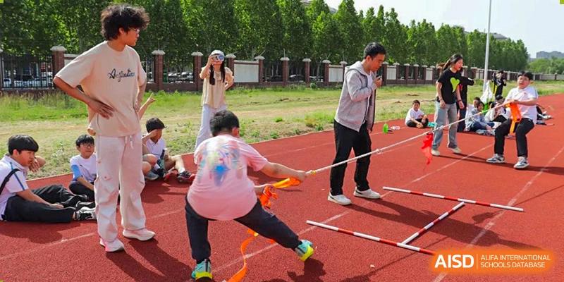 Students participating in a team-building activity involving a rope and an obstacle on a red running track at Glocal Elite International School.
