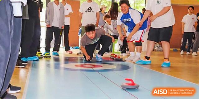 A student crouching down to push a stone in a game of floor curling while surrounded by teammates at Glocal Elite International School.