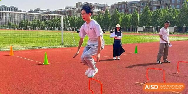 A student leaping over a small orange hurdle during a track and field activity on a sunny day at Glocal Elite International School.