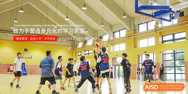 A group of students playing basketball on an indoor court, framed by a poster encouraging a good learning atmosphere at Glocal Elite International School.