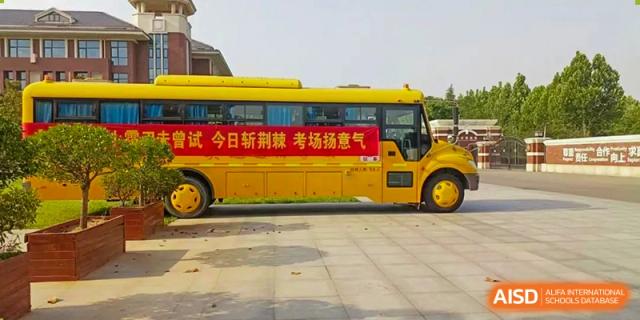 A bright yellow school bus with a banner in Chinese promoting study and exams, parked outside the Glocal Elite International School.