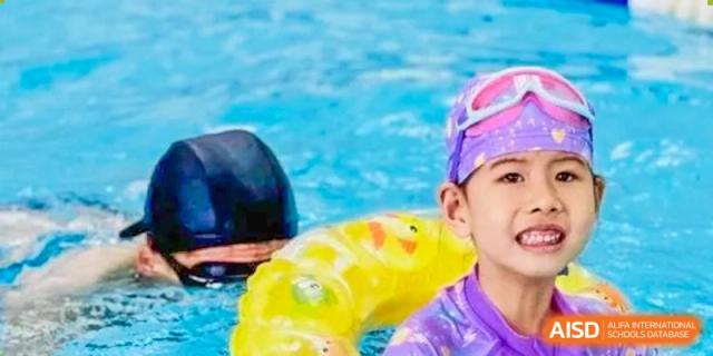 A close-up of a student in a swimming cap and goggles with a yellow inflatable device, possibly during a lesson or competition at Glocal Elite International School.