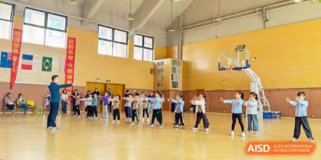 A group of students performing a synchronized group exercise or dance routine on a bright wooden floor in the gymnasium at Glocal Elite International School.