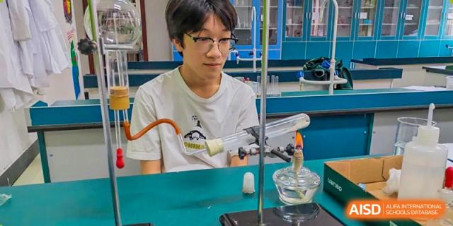 A male student observing a science experiment involving a glass apparatus and a flame in a laboratory at Maple Leaf International School-Zhenjiang.