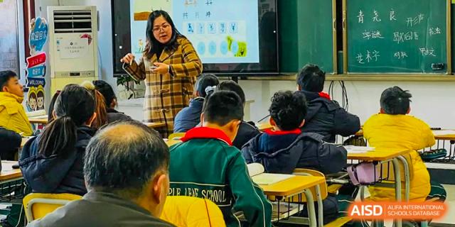 A teacher pointing to a presentation on a screen while instructing students in a brightly lit classroom at Maple Leaf International School-Zhenjiang.